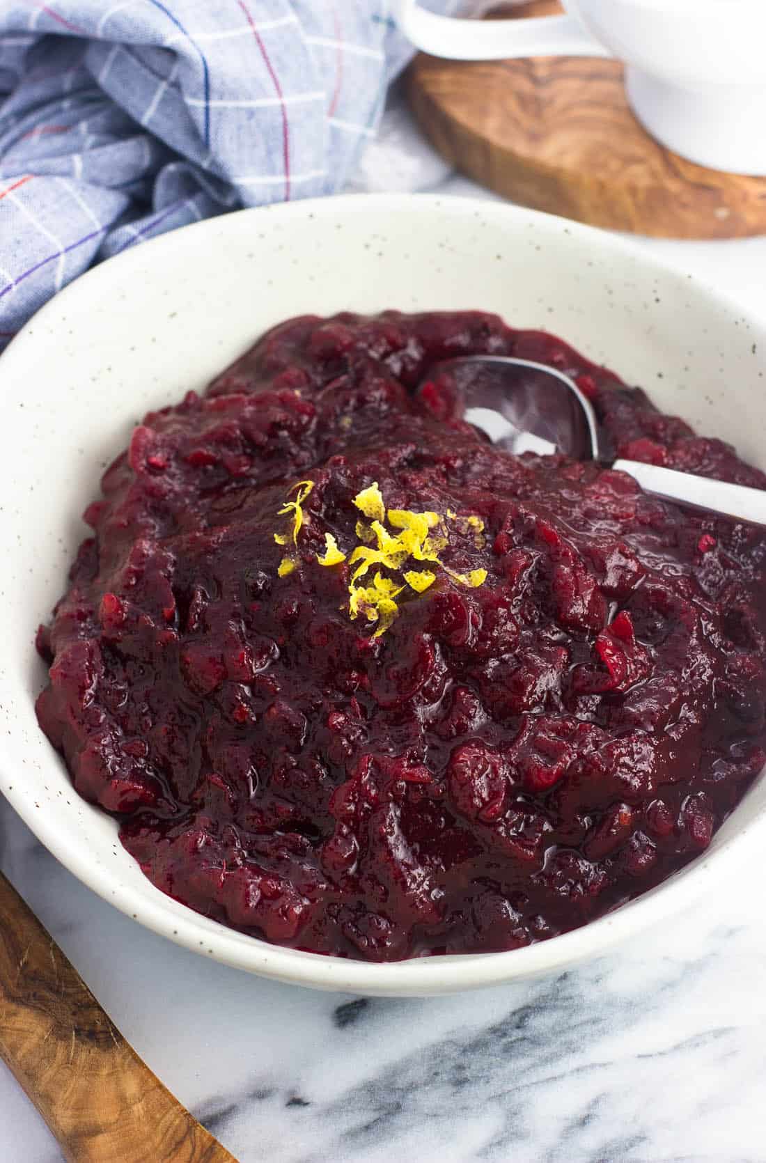 Cranberry sauce in a serving dish with a spoon topped with zest