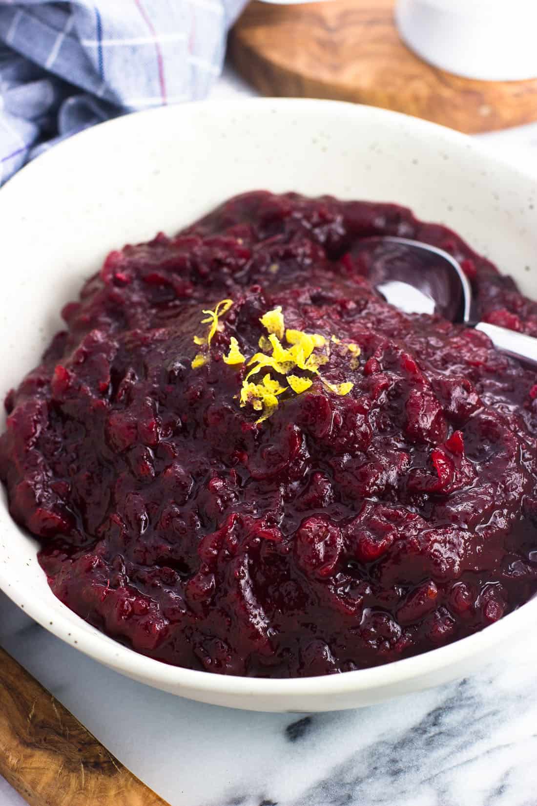 Cranberry sauce in a serving dish with a spoon topped with citrus zest