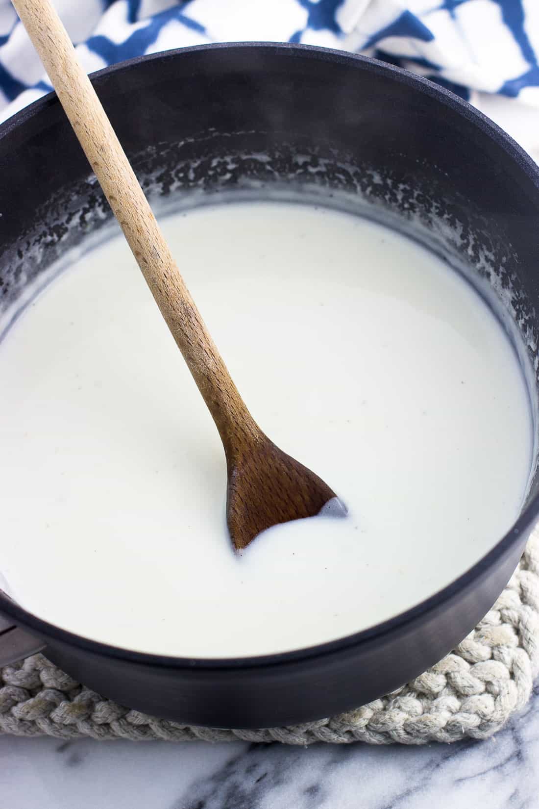 Healthy alfredo sauce in a saucepan with a wooden spoon after thickening.