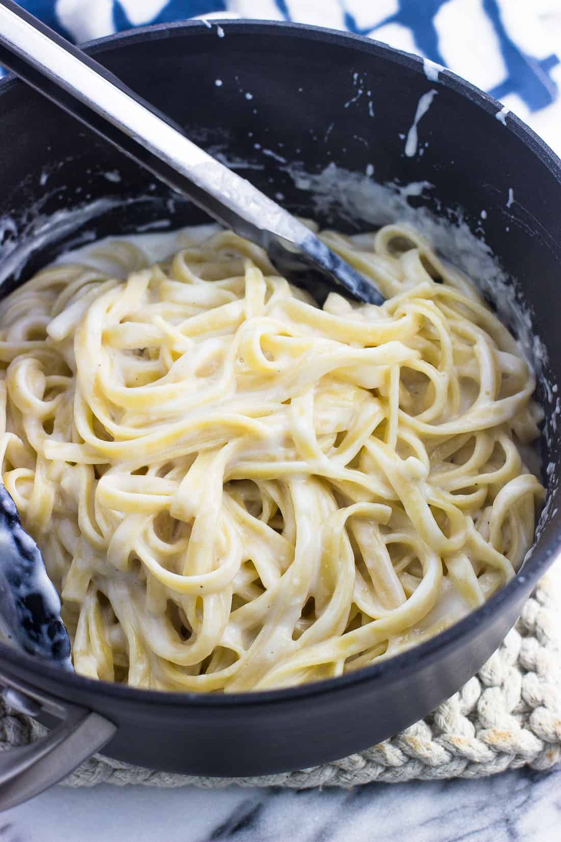 Fettuccine being tossed in alfredo sauce with tongs.