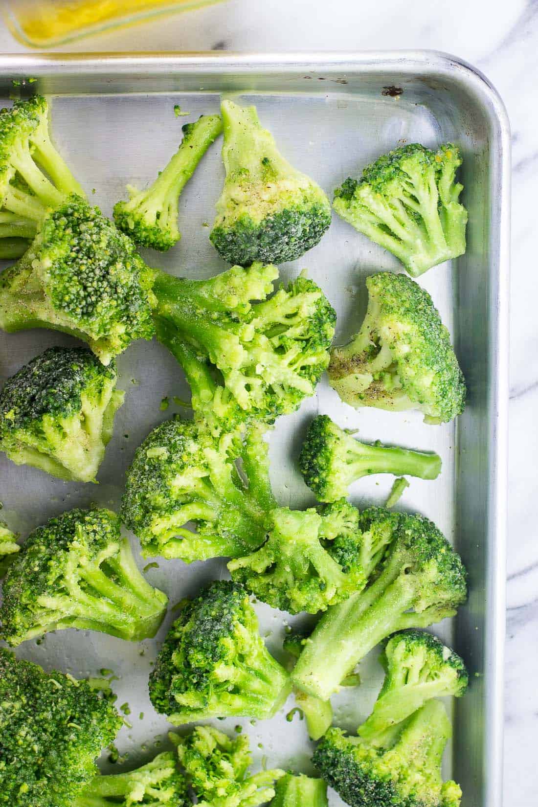 Broccoli florets tossed with olive oil and spices on a sheet pan ready for the oven.