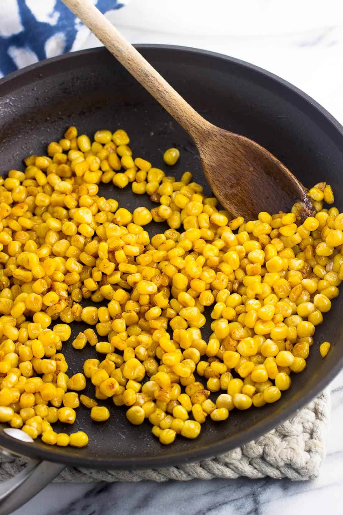 Roasted corn kernels in a skillet with a wooden spoon