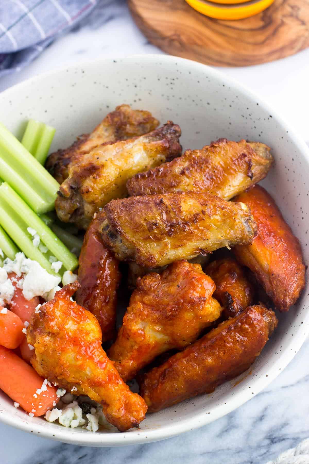 A bowl filled with chicken wings (half plain and half coated in hot sauce) with celery, carrots, and blue cheese.