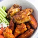 A bowl filled with chicken wings (half plain and half coated in hot sauce) with celery sticks, baby carrots, and crumbled blue cheese