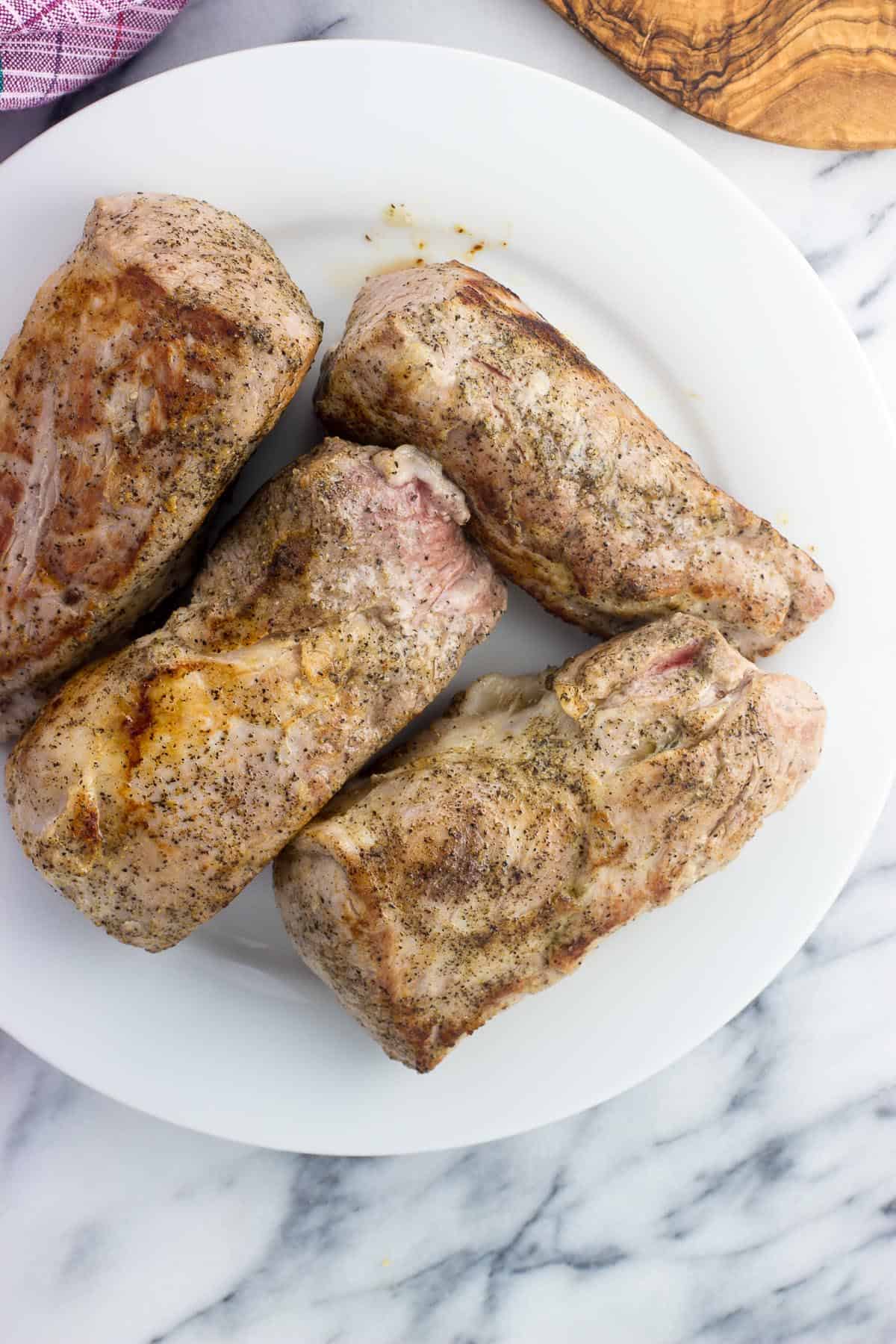 Seared pork tenderloin halves on a plate.