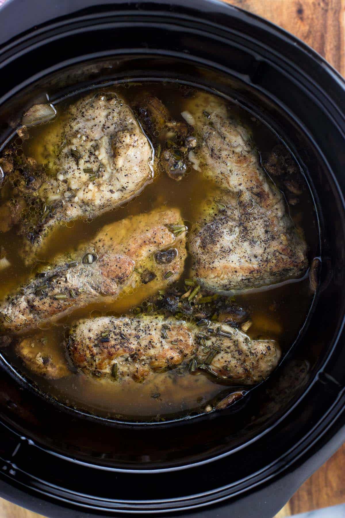 An overhead shot of the pork tenderloin in the slow cooker once cooked, before thickening the balsamic rosemary sauce.