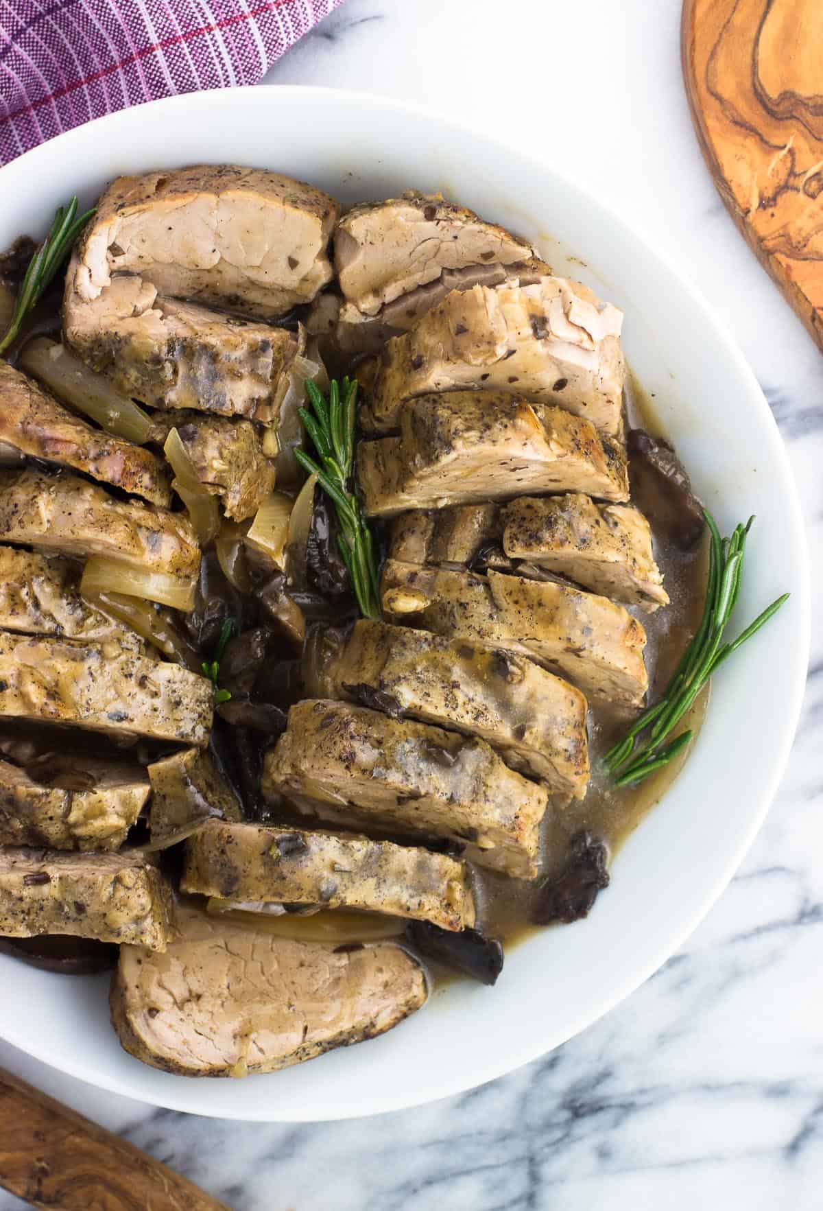 Sliced pork tenderloin in a serving dish with sauce and rosemary sprigs.