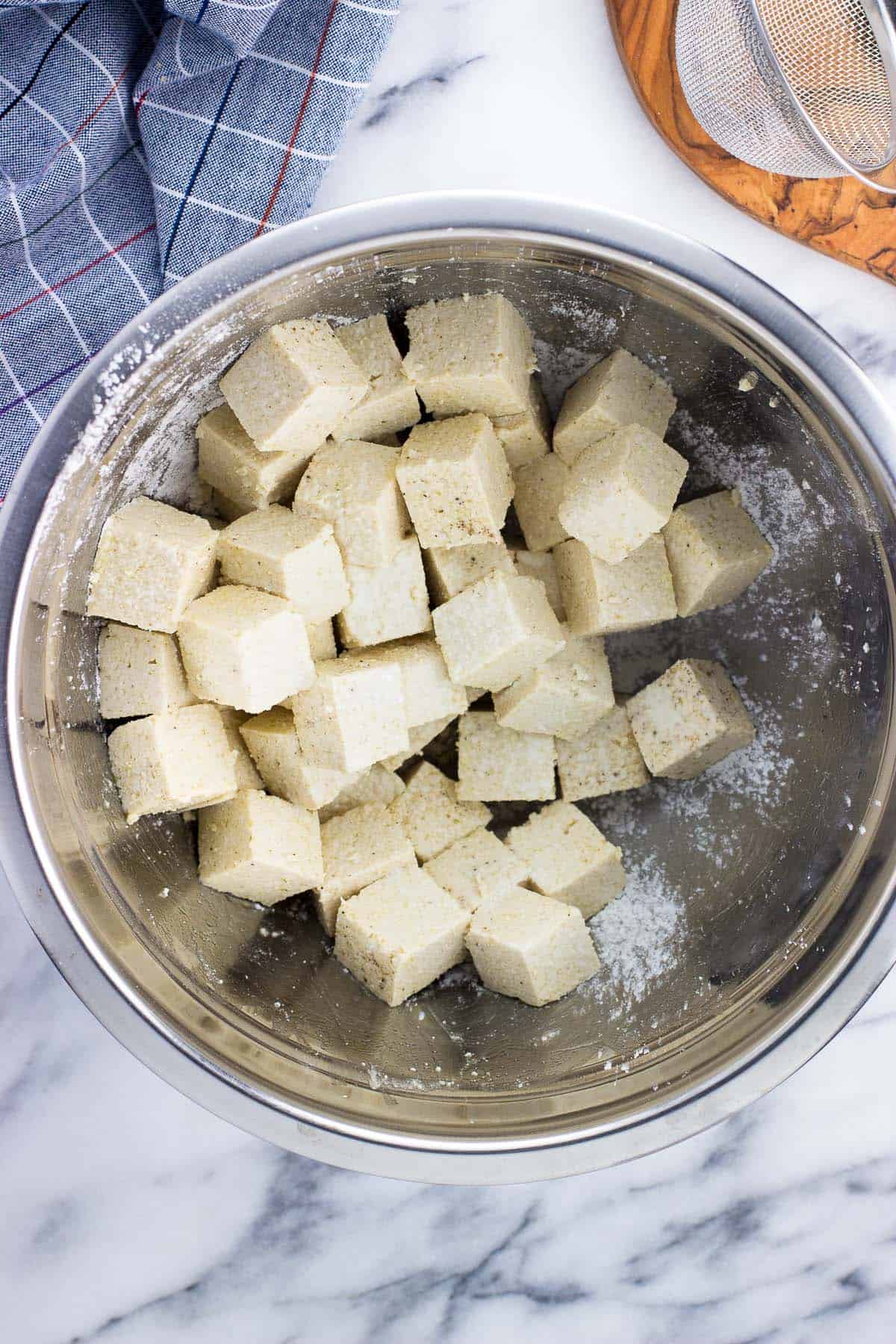 An overhead picture of tofu cubes tossed in cornstarch and spices in a metal mixing bowl.