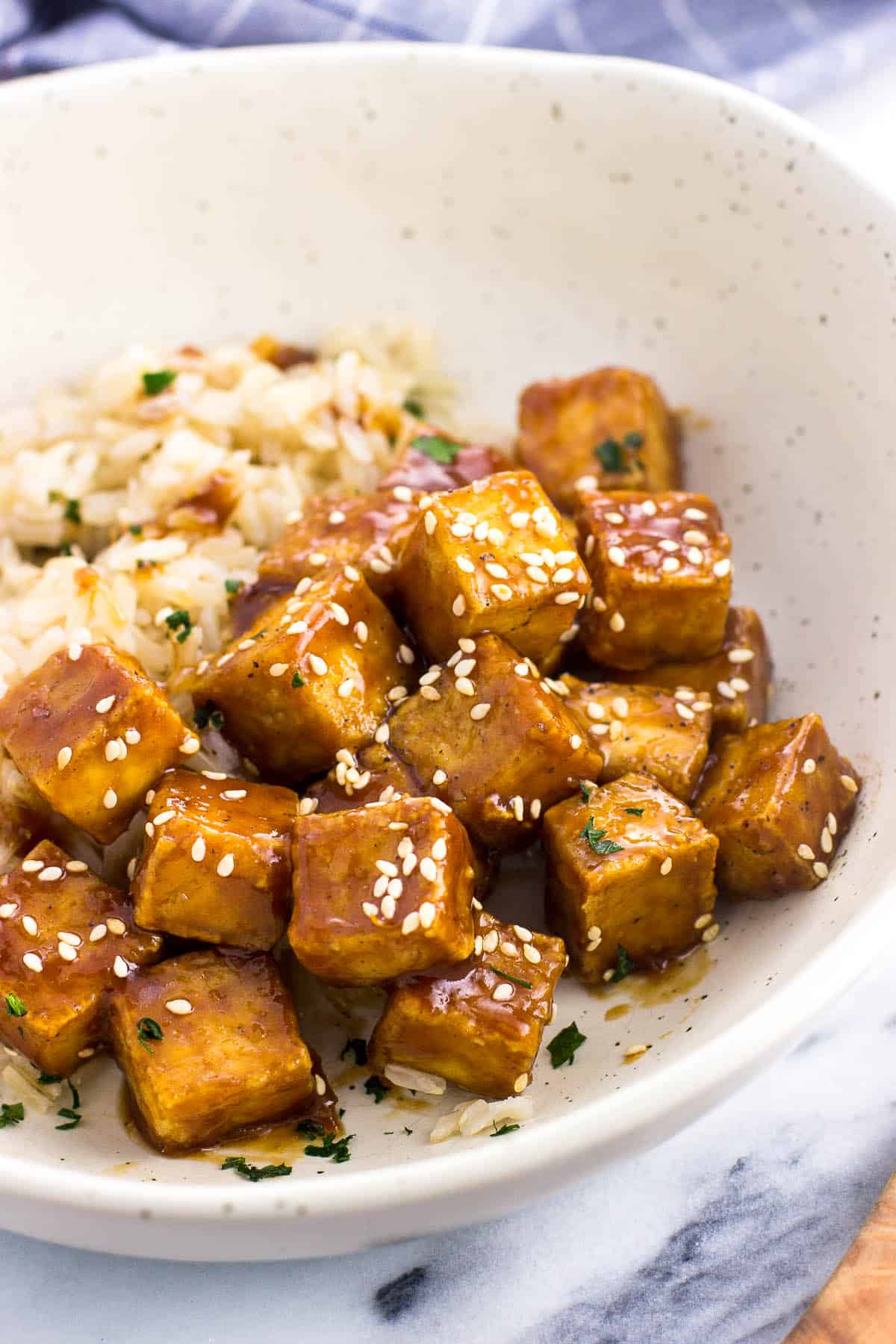 Cubes of tofu tossed in glaze and topped with sesame seeds in a bowl with brown rice.