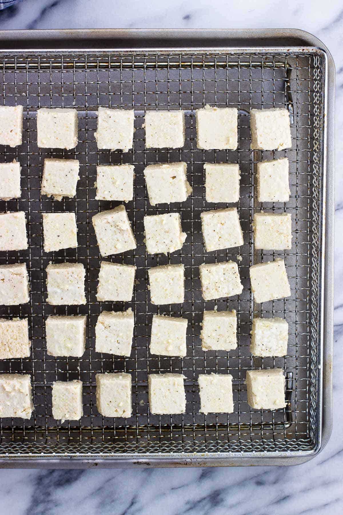 Tofu cubes lined up in a single layer on a metal air fryer basket.