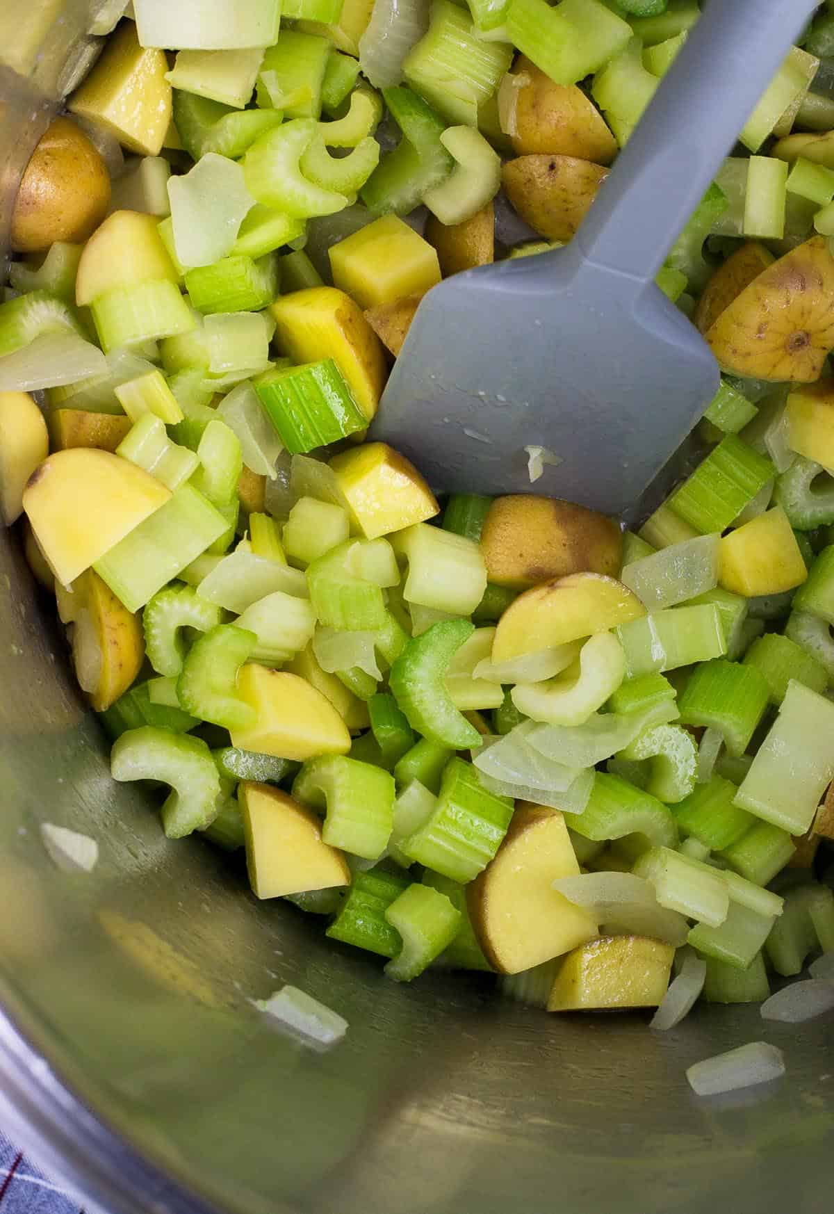 Chopped celery, potato, onion, and garlic in a soup pot with a spatula