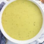 A stoneware pot of creamy celery soup next to a dish towel