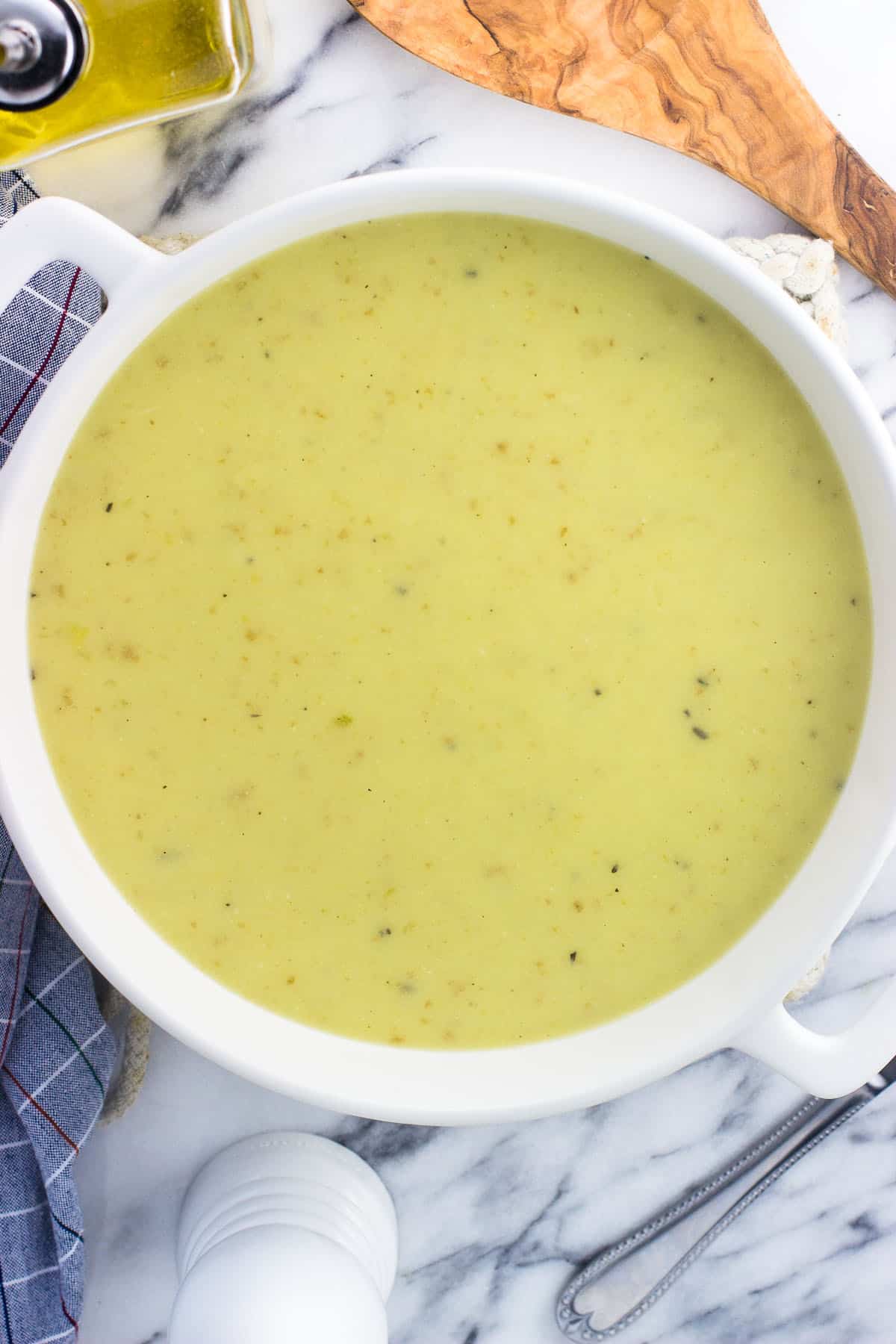 A stoneware pot of creamy celery soup next to a dish towel.