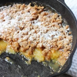 A peach crisp with a thick crumb topping in a round cast iron pan