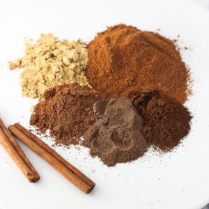 Five mounds of dried spices before being mixed together in a pie spice blend