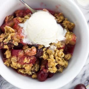 An overhead shot of a bowl of cherry rhubarb crisp with a scoop of vanilla ice cream