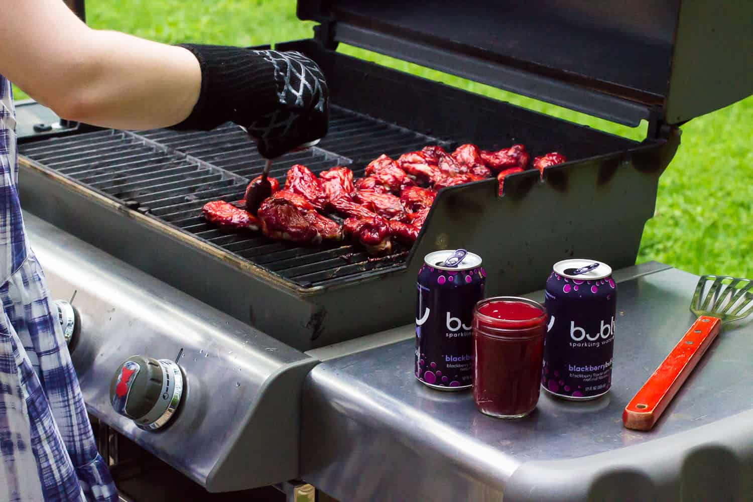 A woman standing at an open grill basting chicken wings with BBQ sauce