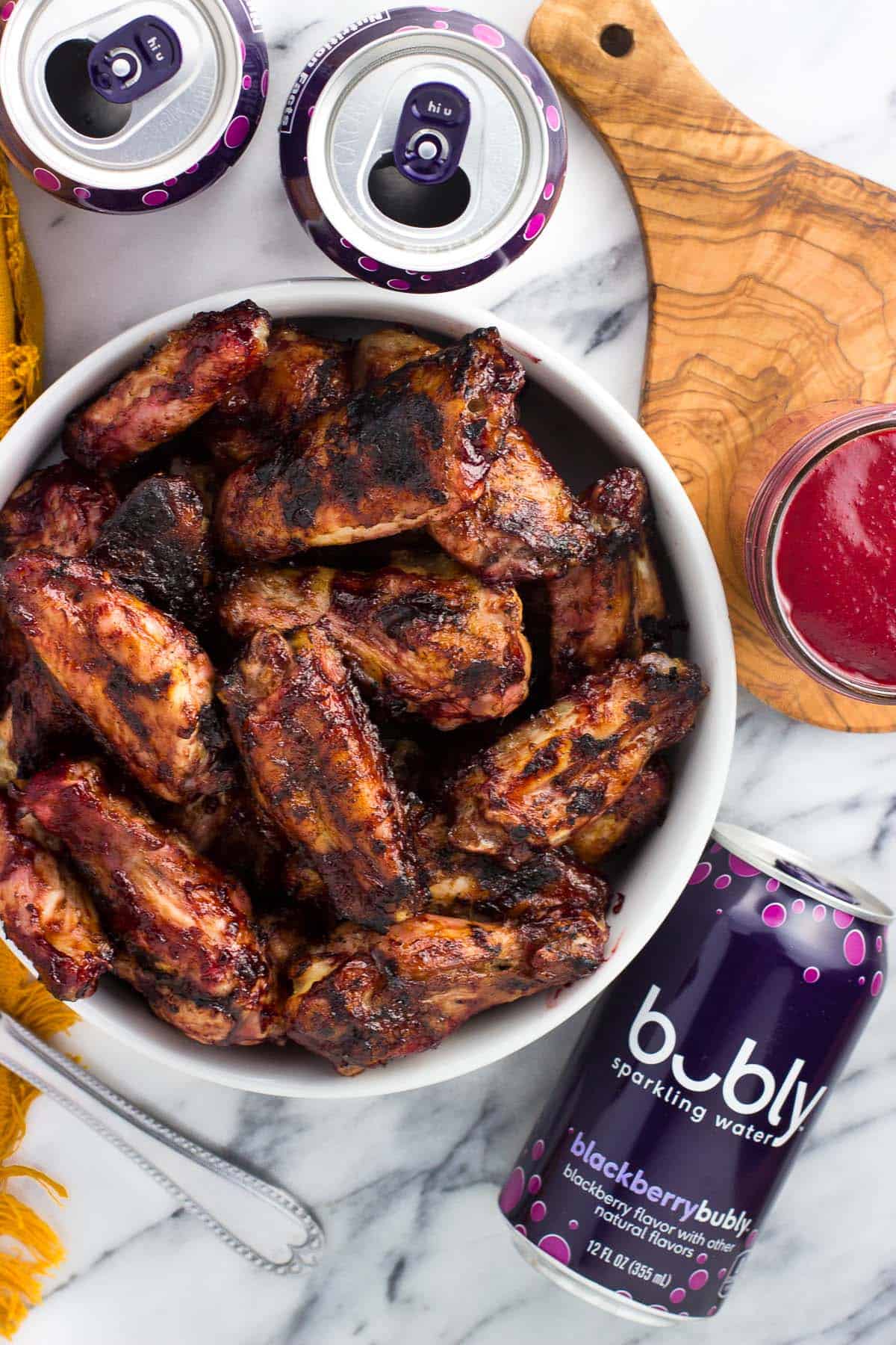 A bowl of grilled wings next to a jar of BBQ sauce and a can of bubly water.