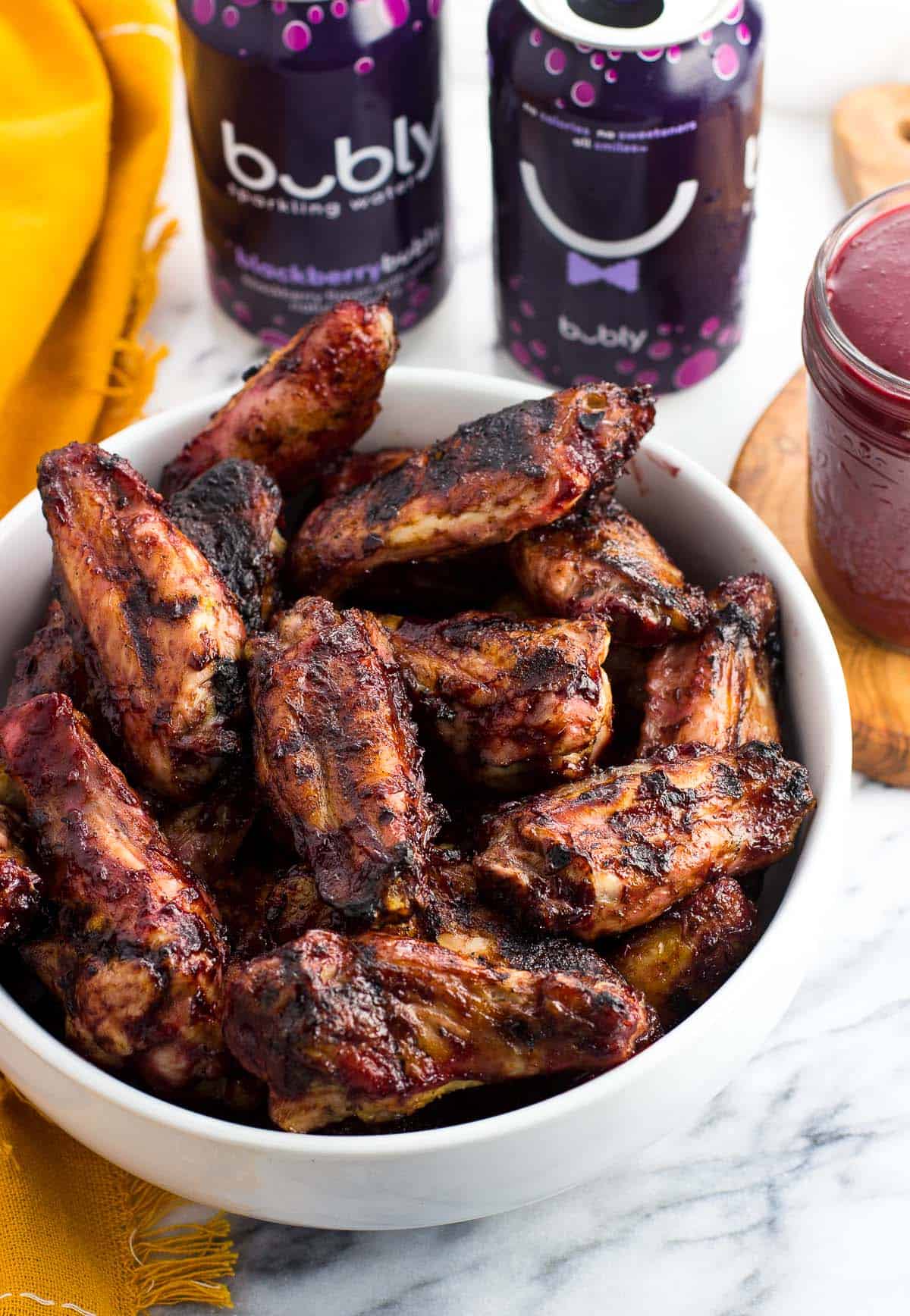 A serving bowl of chicken wings beside two cans of water and a jar of BBQ sauce.