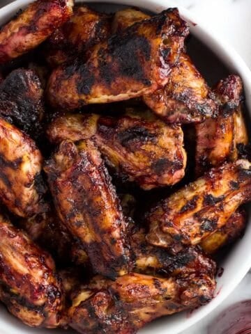 A serving bowl filled with grilled chicken wings next to a glass jar filled with BBQ sauce