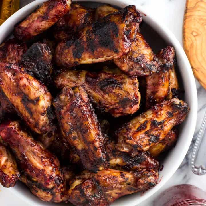 A serving bowl filled with grilled chicken wings next to a glass jar filled with BBQ sauce