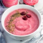 A smoothie bowl with raspberries, flaxseed, and chia seeds next to two cans of water.