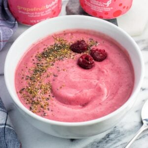 A smoothie bowl with raspberries, flaxseed, and chia seeds next to two cans of water.