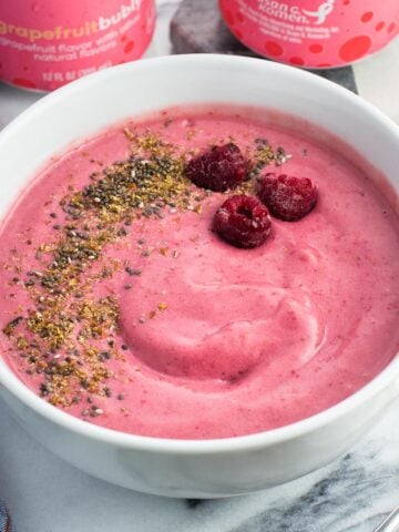 A smoothie bowl with raspberries, flaxseed, and chia seeds next to two cans of water.