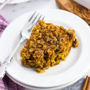 A square oatmeal bar on a small dessert plate with a fork with a bite taken out of it. Another serving is on a plate in the background