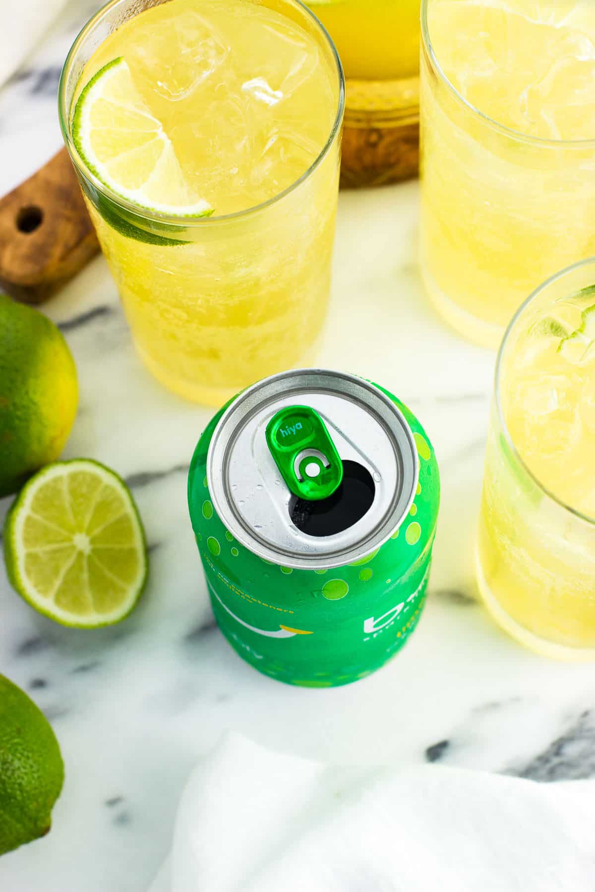 An open can of lime bubly water next to glasses of mocktails and cut limes.