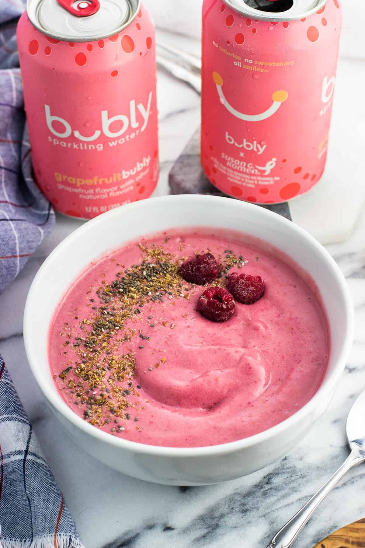 A smoothie bowl with raspberries, flaxseed, and chia seeds next to two cans of water.