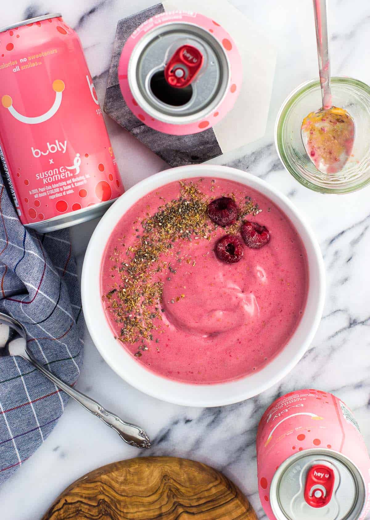 A smoothie bowl next to cans of bubly water and spoons.