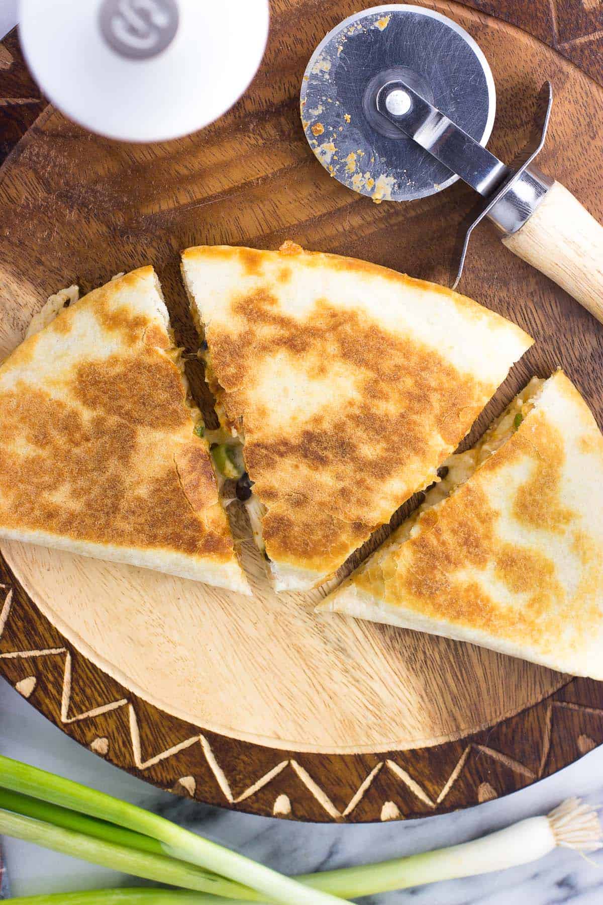 A folded and cooked tortilla on a wooden board sliced into three even wedges, next to a pizza cutter