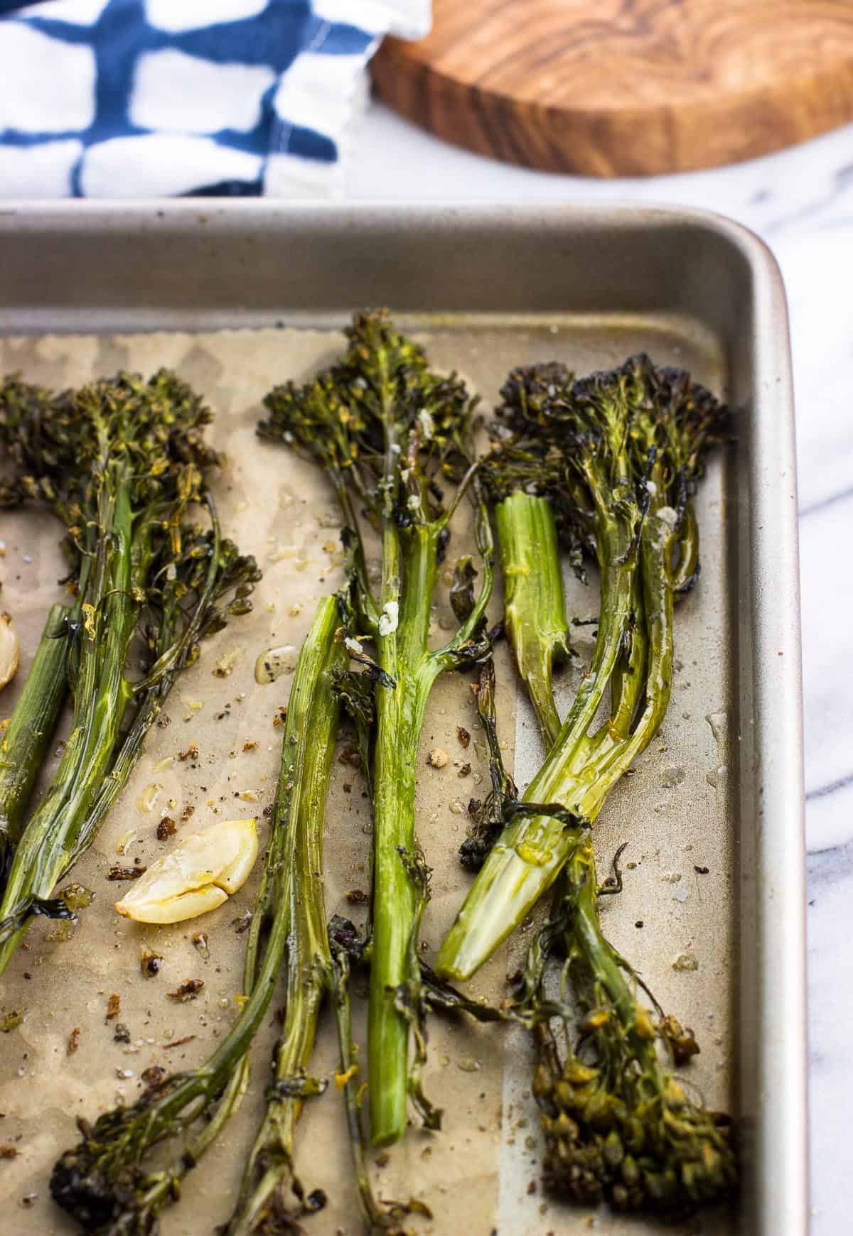 Roasted broccolini spears and garlic cloves on a parchment-lined baking sheet.