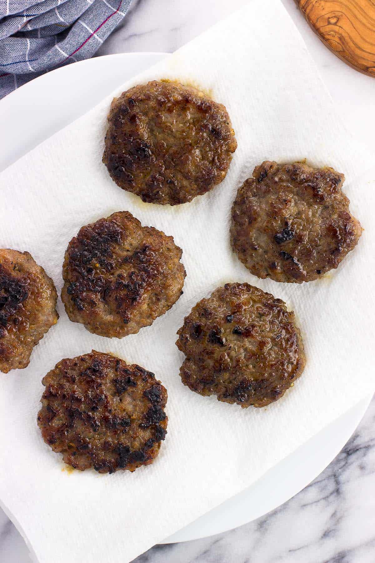 Cooked sausage patties draining on a paper-towel lined plate