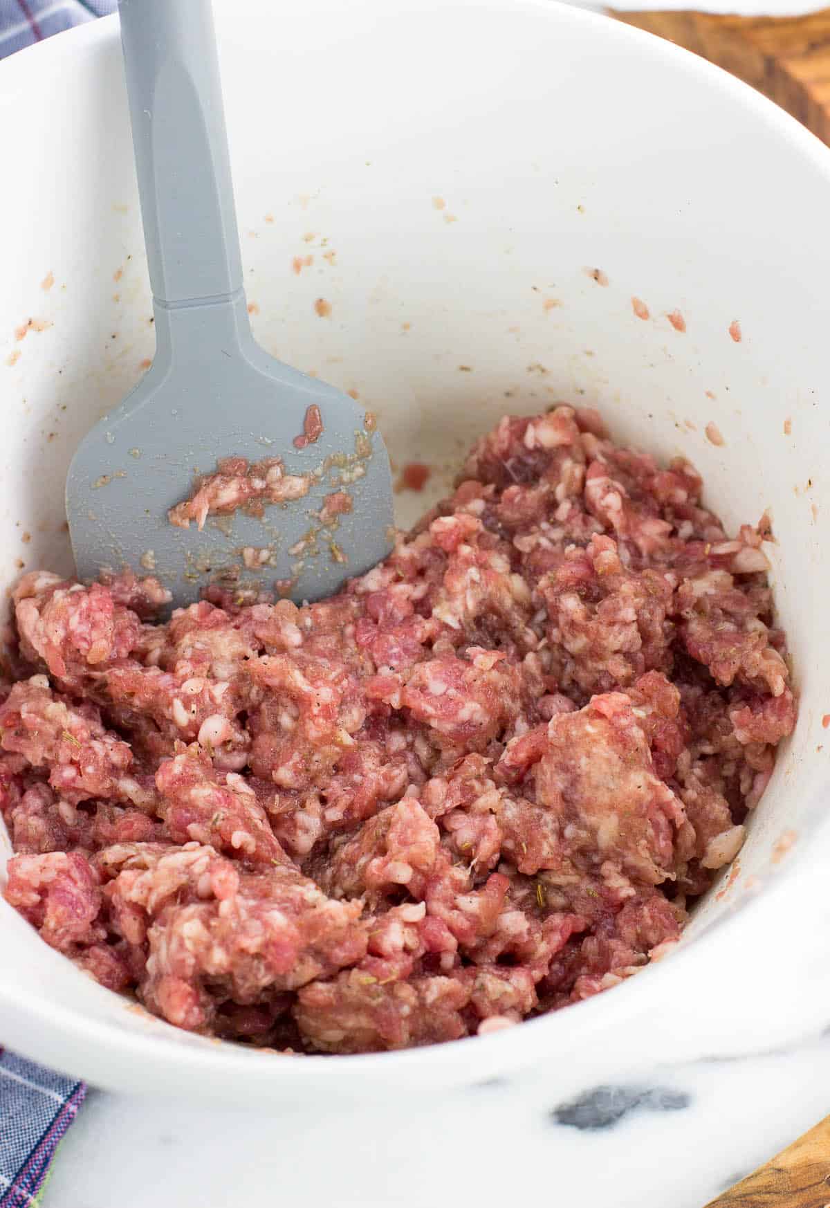 A mixing bowl with a spatula stuck in the ground pork mixture after it has been combined with the other ingredients