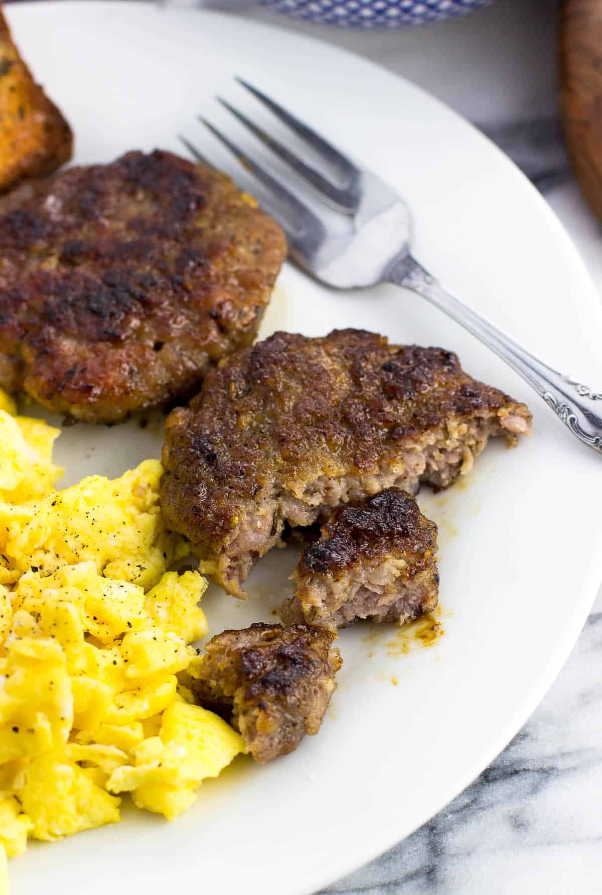 A sausage patty cut in half on a plate with scrambled eggs and another full patty