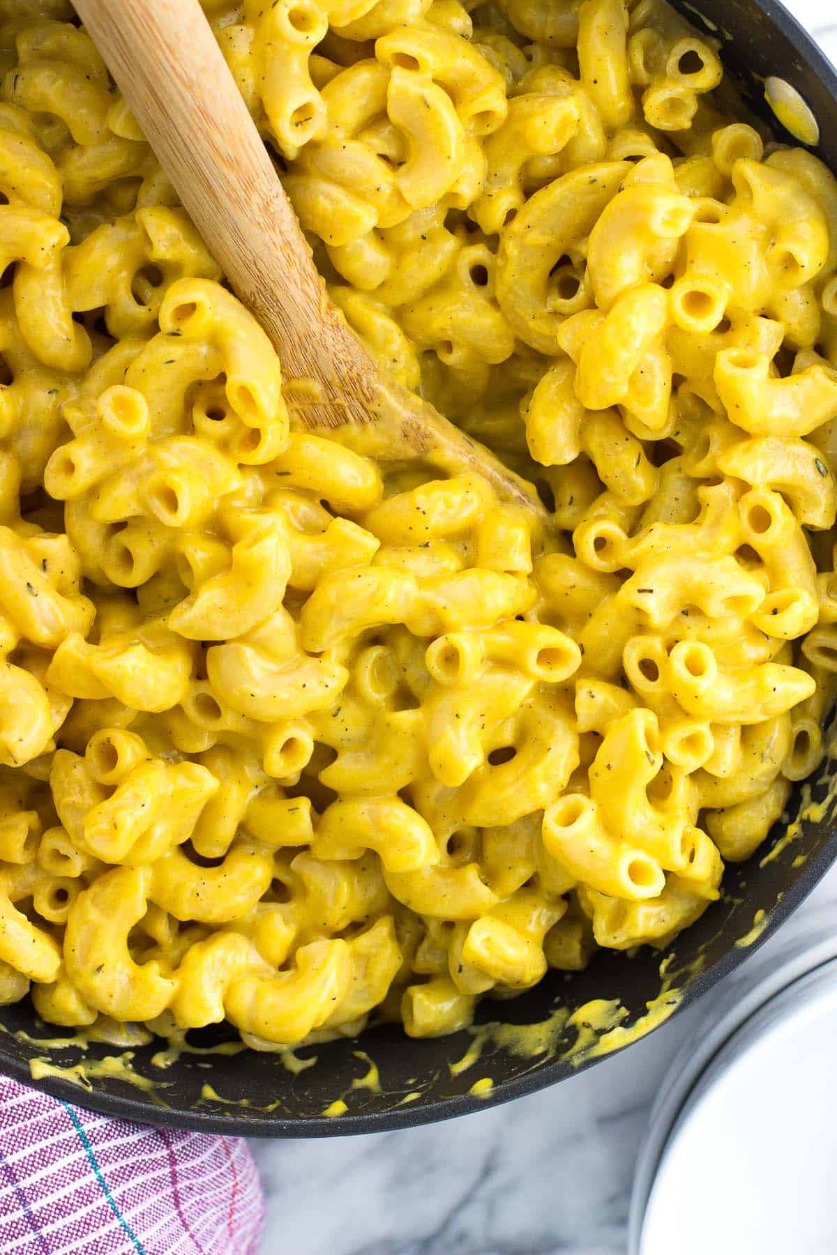 Mac and cheese in a skillet with a wooden spoon scooped in