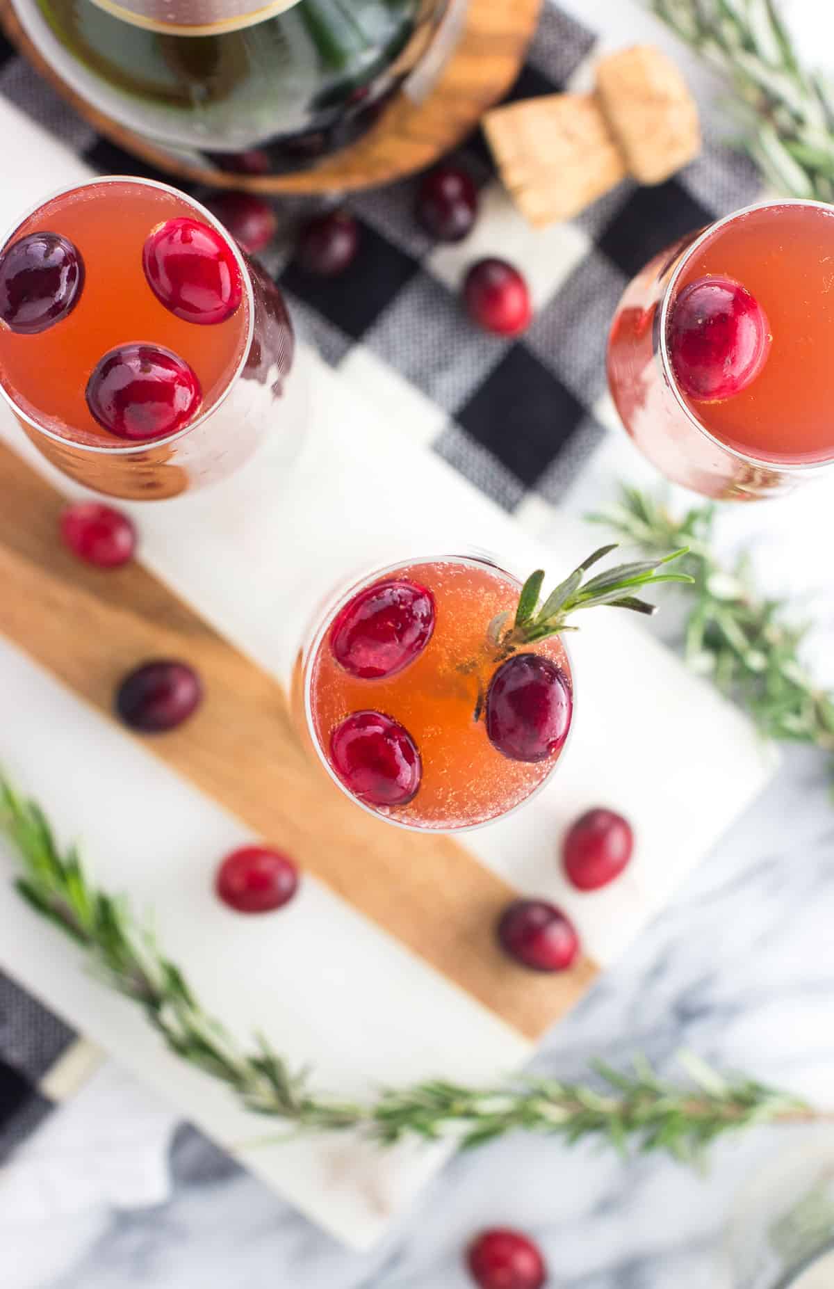 An overhead picture of mimosas in flutes garnished with fresh cranberries and rosemary sprigs.