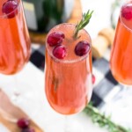 A cranberry mimosa in a champagne flute garnished with cranberries and fresh rosemary