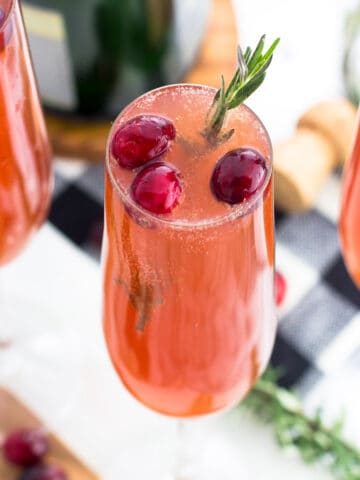 A cranberry mimosa in a champagne flute garnished with cranberries and fresh rosemary