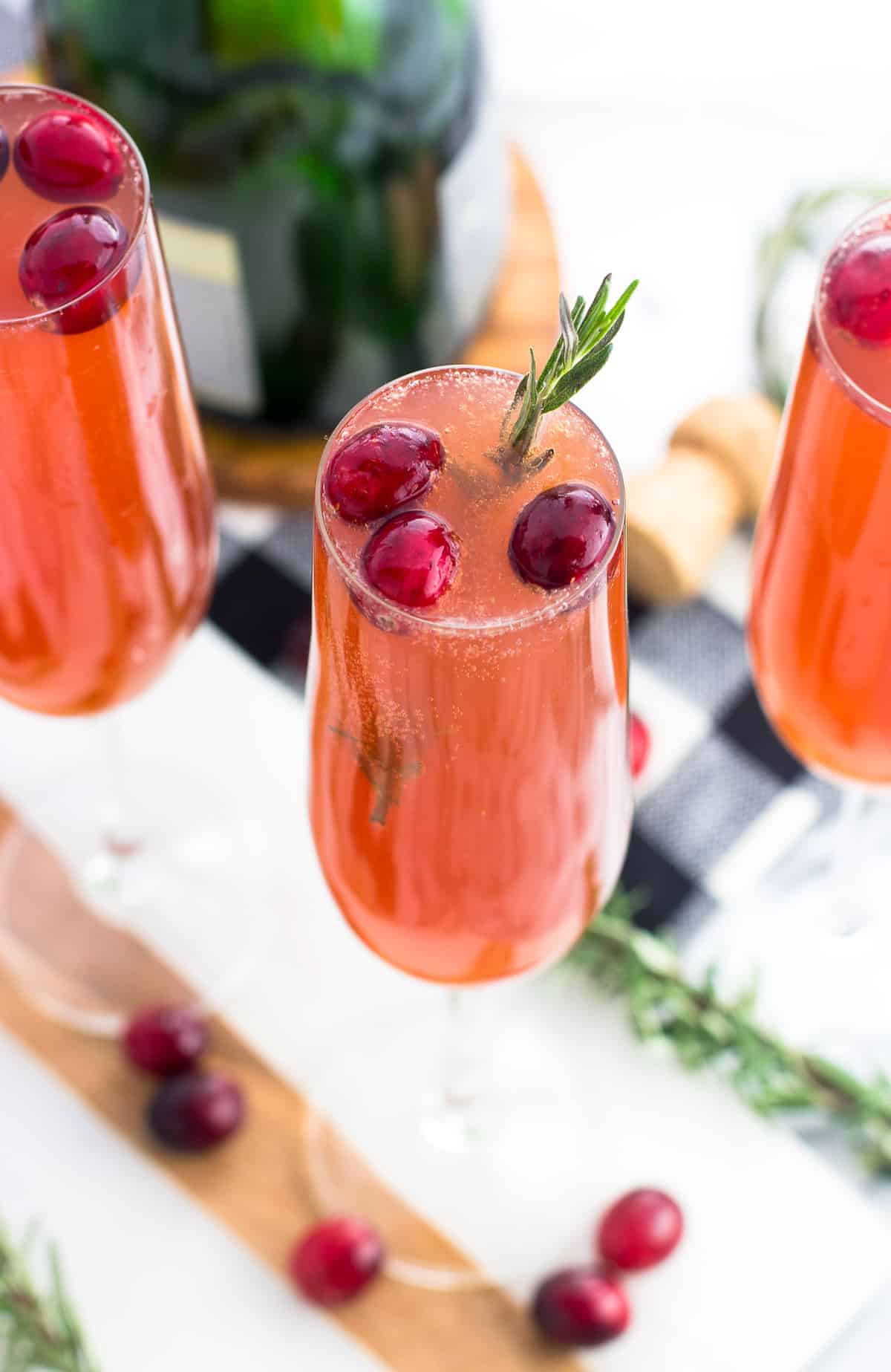 Three cranberry mimosas garnished with cranberries and rosemary sprigs.