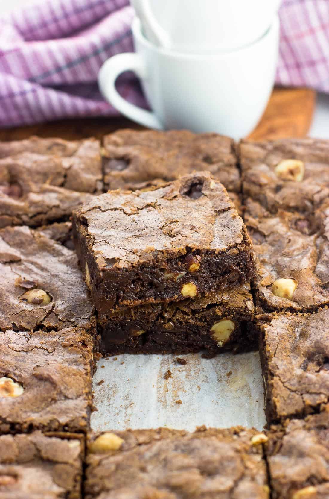 A pan of chocolate hazelnut brownies cut into squares with two brownies stacked on top of one another.