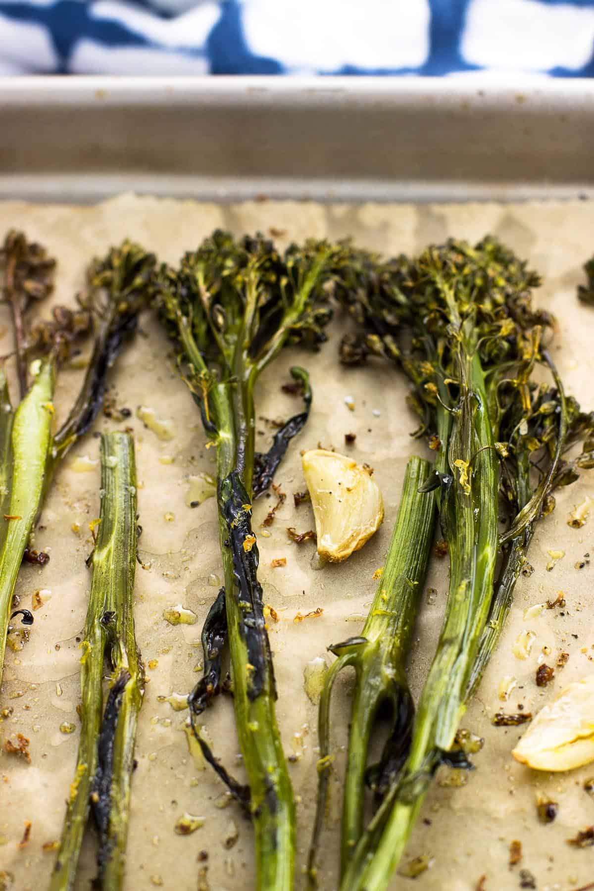 Broccolini and whole garlic cloves roasted on a parchment-lined baking sheet.