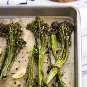 Roasted broccolini spears and garlic cloves on a parchment-lined baking sheet.