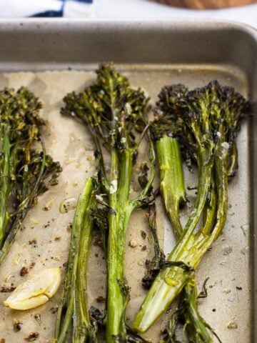 Roasted broccolini spears and garlic cloves on a parchment-lined baking sheet.