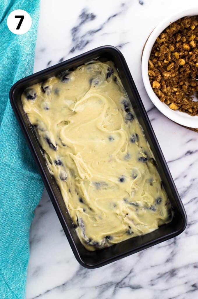 Batter poured into a loaf pan next to a bowl of streusel.