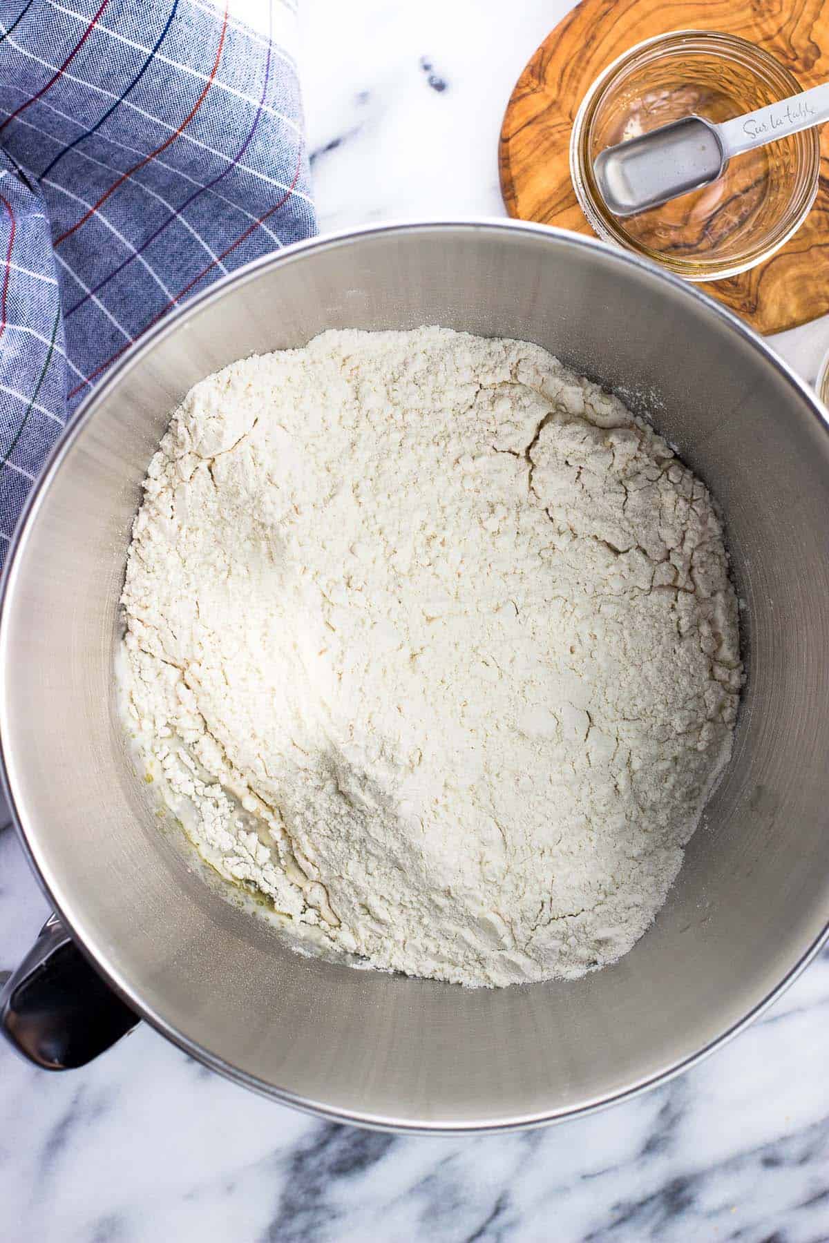 Flour, olive oil, salt, and sugar added to the water and yeast in a bowl.