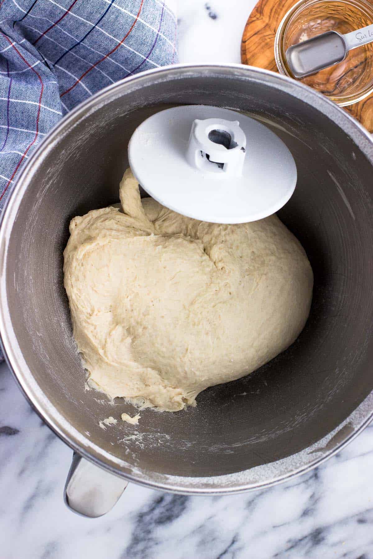 Pizza dough in a metal stand mixer bowl with the dough hook.