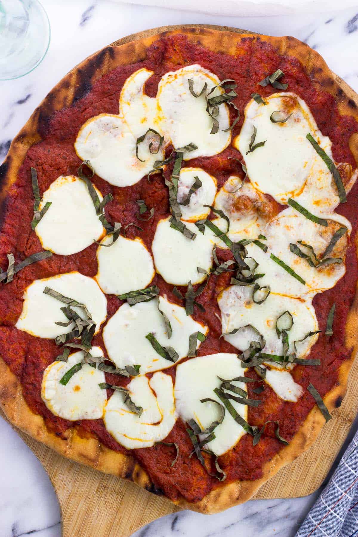 A grilled pizza on a wooden pizza peel.